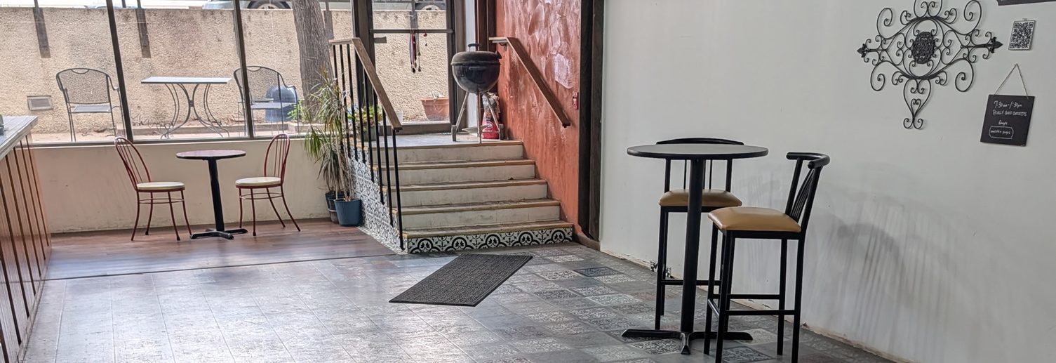 Inside Omelette Pages: cafe tables by the windows, patterned tile floor, and the steps up to the entry
