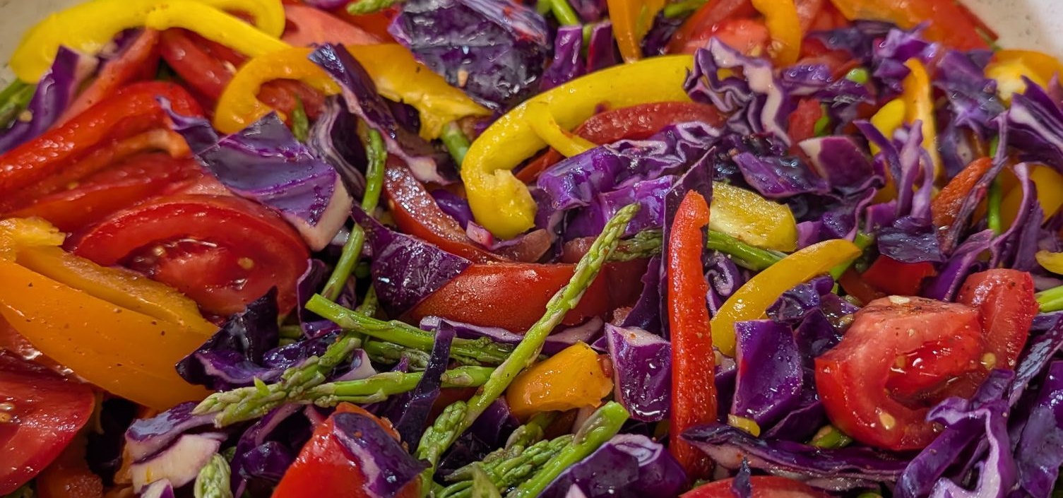 A pan of sauteed red cabbage, asparagus, tomatoes and sweet peppers